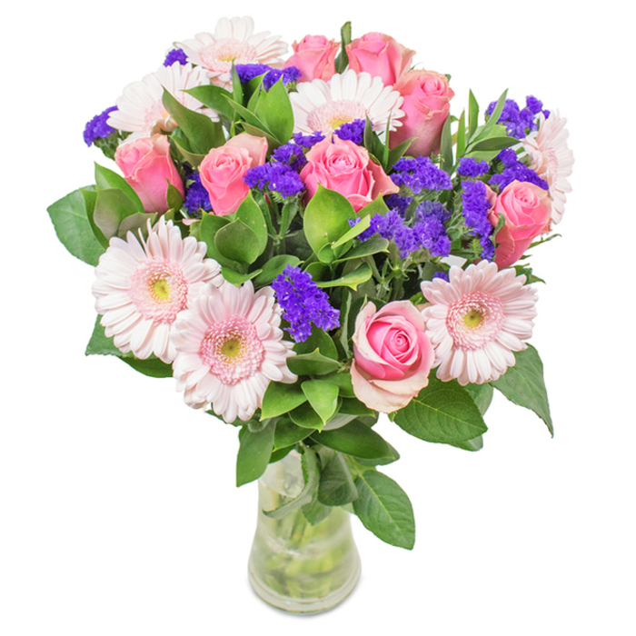 Presented in a crystal-clear glass vase and set before a crisp white backdrop, this vibrant bouquet by Florist Camberwell captures the harmony of local artistry. At its centre, approximately 7-9 classic pink roses are arranged with precision, their tightly spiralled petals hinting at elegance and anticipation-a nod to Camberwell's refined Georgian avenues. Around them, 5-7 pale pink gerbera daisies radiate gentle charm, their dainty heads open wide to reveal soft, nearly white centres, echoing the delicate pastels seen through springtime windows along Coldharbour Lane. Contrasting these gentle hues are clusters of vivid purple statice, each tiny bloom adding rich texture and visual depth, much like the creative street murals found nearby. Deep green foliage forms a lavish base, threading freshness and a hint of woodland aroma through the whole arrangement, suggesting a walk in Dulwich Woods. Stems submerged in clear water speak to the bouquet's vitality and readiness for fresh delivery across Camberwell and neighbouring communities. This composition is ideal for a birthday celebration, an anniversary surprise, or a heartfelt thank you-perfect for conveying lasting joy and affection with a local touch.